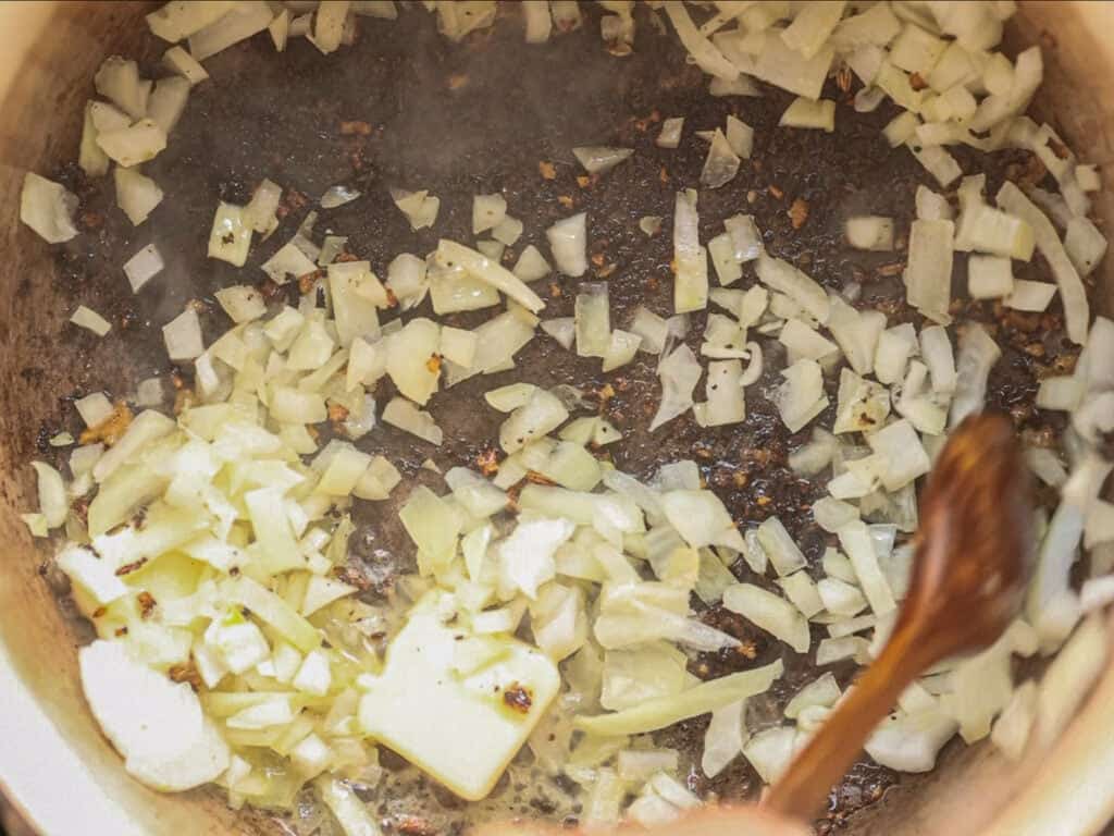Chopped onions being sautéed in a pot, turning translucent and lightly browned, with a wooden spoon stirring them.